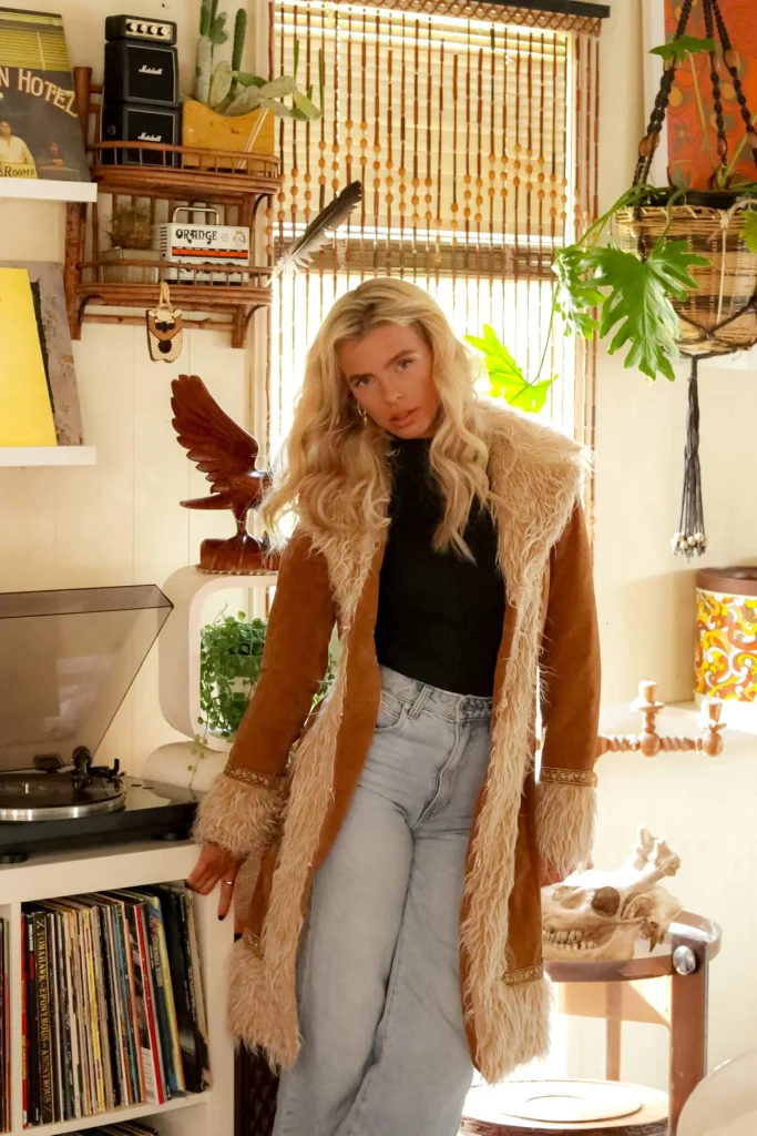 Blond woman in fur coat in brightly colored room with plants.