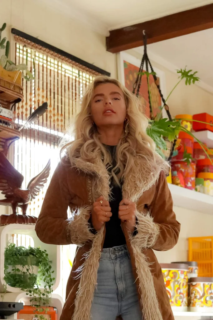 Blond woman in fur coat in brightly colored room with plants.