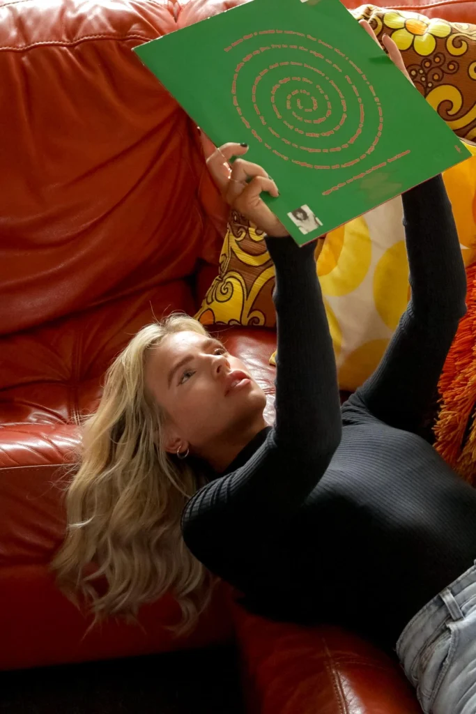 Blond woman laying on red couch and holding a record.