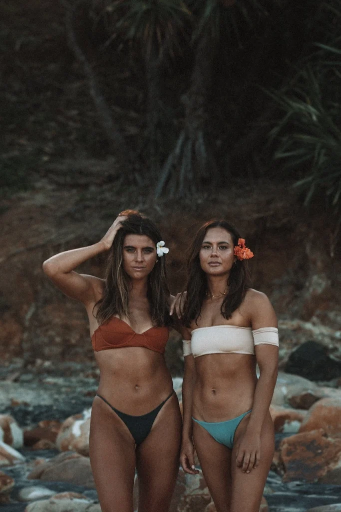 Two dark-haired women in colorful bikinis on the beach.