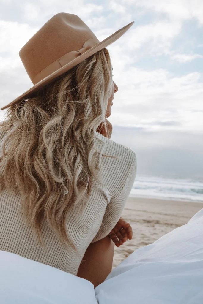 Blond woman wearing a hat and laying on the beach.