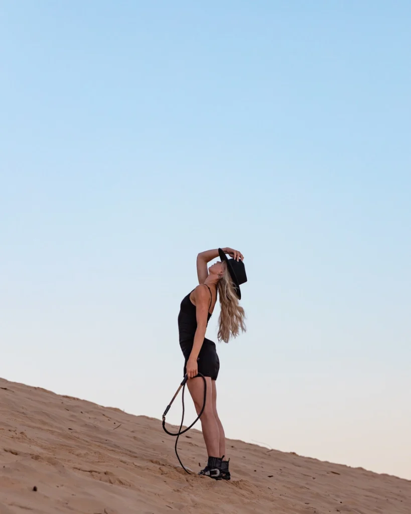 Blond woman in a black hat on sand dunes.