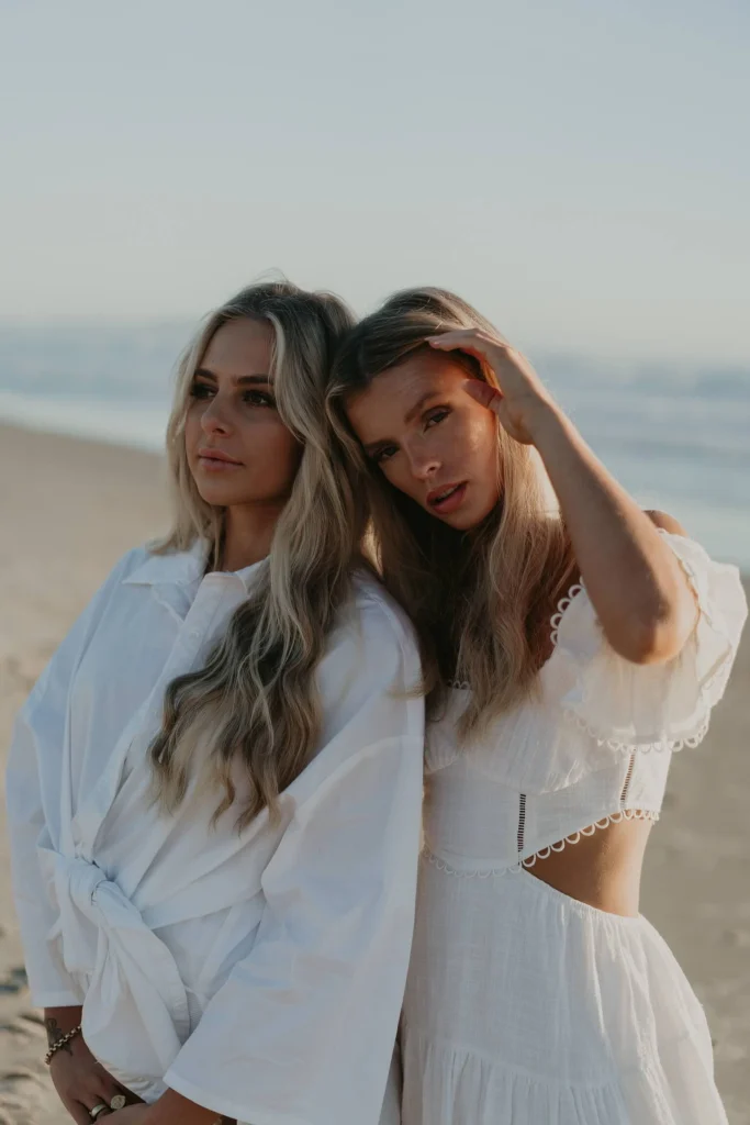 Two blond women in white dresses on the beach.